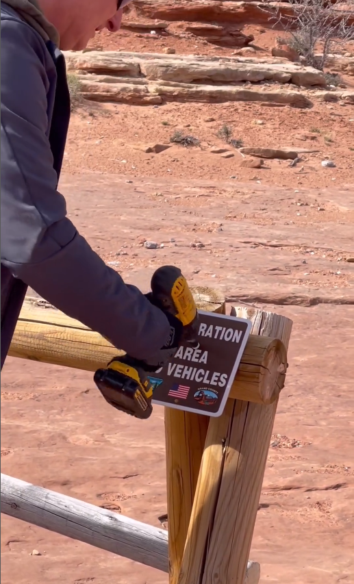 Person drilling sign to fence post